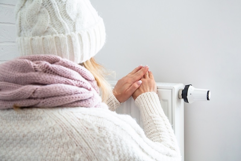 жена облечена в зимни дрехи топли ръцете си на радиатор